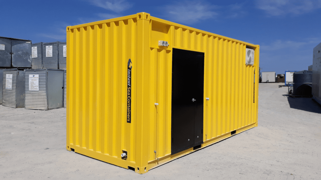 Bright yellow shipping container converted into a small office, featuring a black door and an air conditioning unit, placed in an outdoor storage yard.