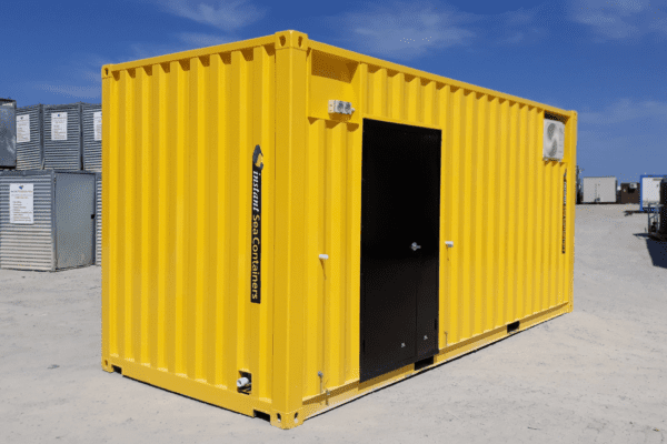 Bright yellow shipping container converted into a small office, featuring a black door and an air conditioning unit, placed in an outdoor storage yard.