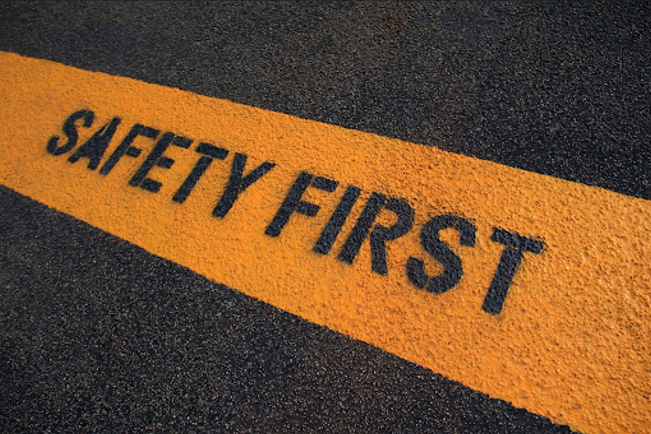 Close-up view of a yellow line on asphalt with the words 'SAFETY FIRST' stenciled in black.