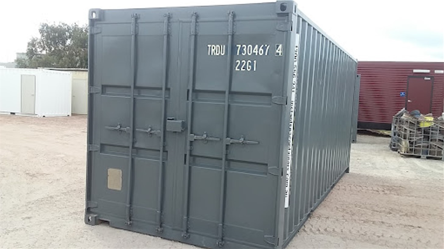 Gray shipping container with double doors closed, situated in a storage yard with other containers in the background.