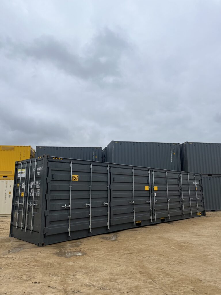 Large black 40’HC Side Opening Container on a dirt lot under cloudy skies.