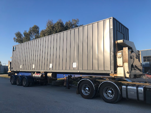 Large gray shipping container mounted on a flatbed trailer, ready for transportation at dusk.