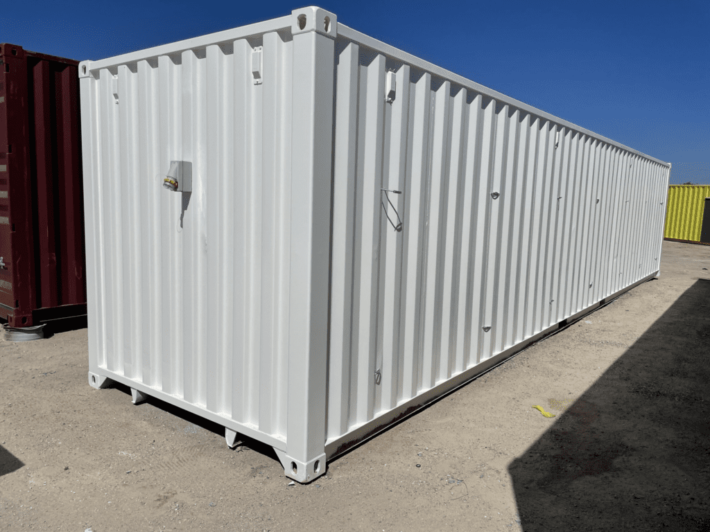 White shipping container with a single door and two windows, set against a clear blue sky.