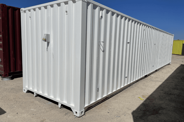 White shipping container with a single door and two windows, set against a clear blue sky.