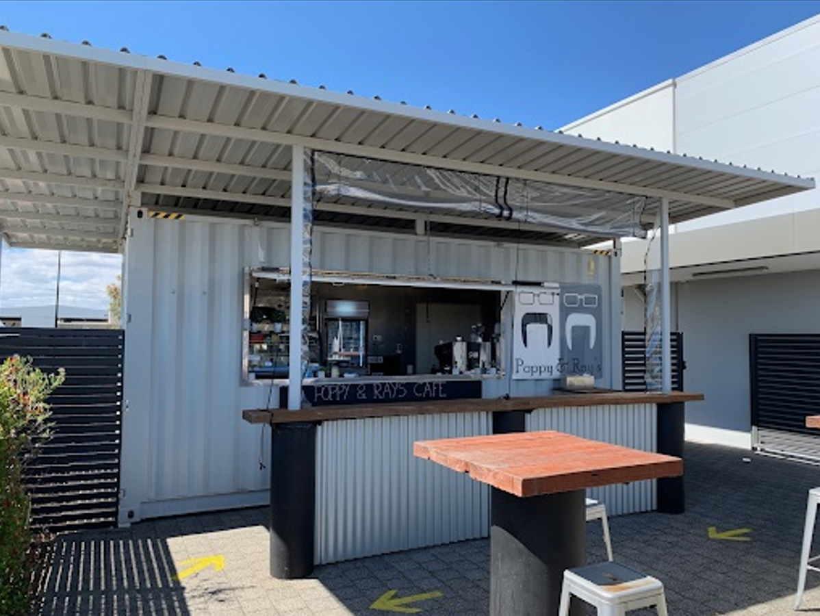 Outdoor café area with a shipping container converted into a coffee shop, featuring a large serving window and covered seating area.