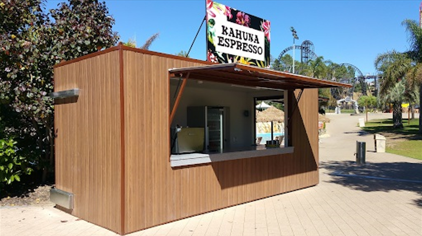 Small outdoor café constructed from a shipping container, featuring a wooden facade and an open serving window under a sign reading 'Kahuna Espresso'.