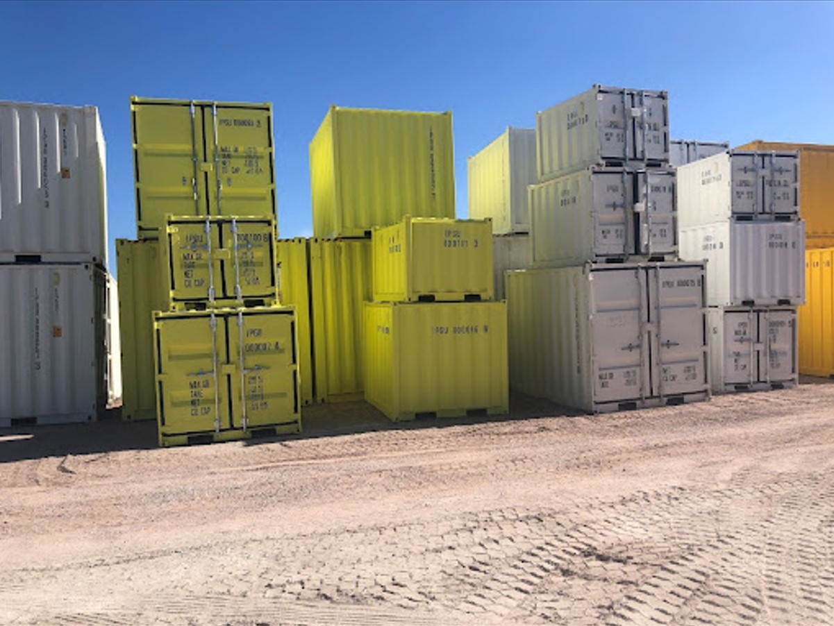 Stacked colorful shipping containers in yellow, green, and white on a gravel lot under clear blue skies.