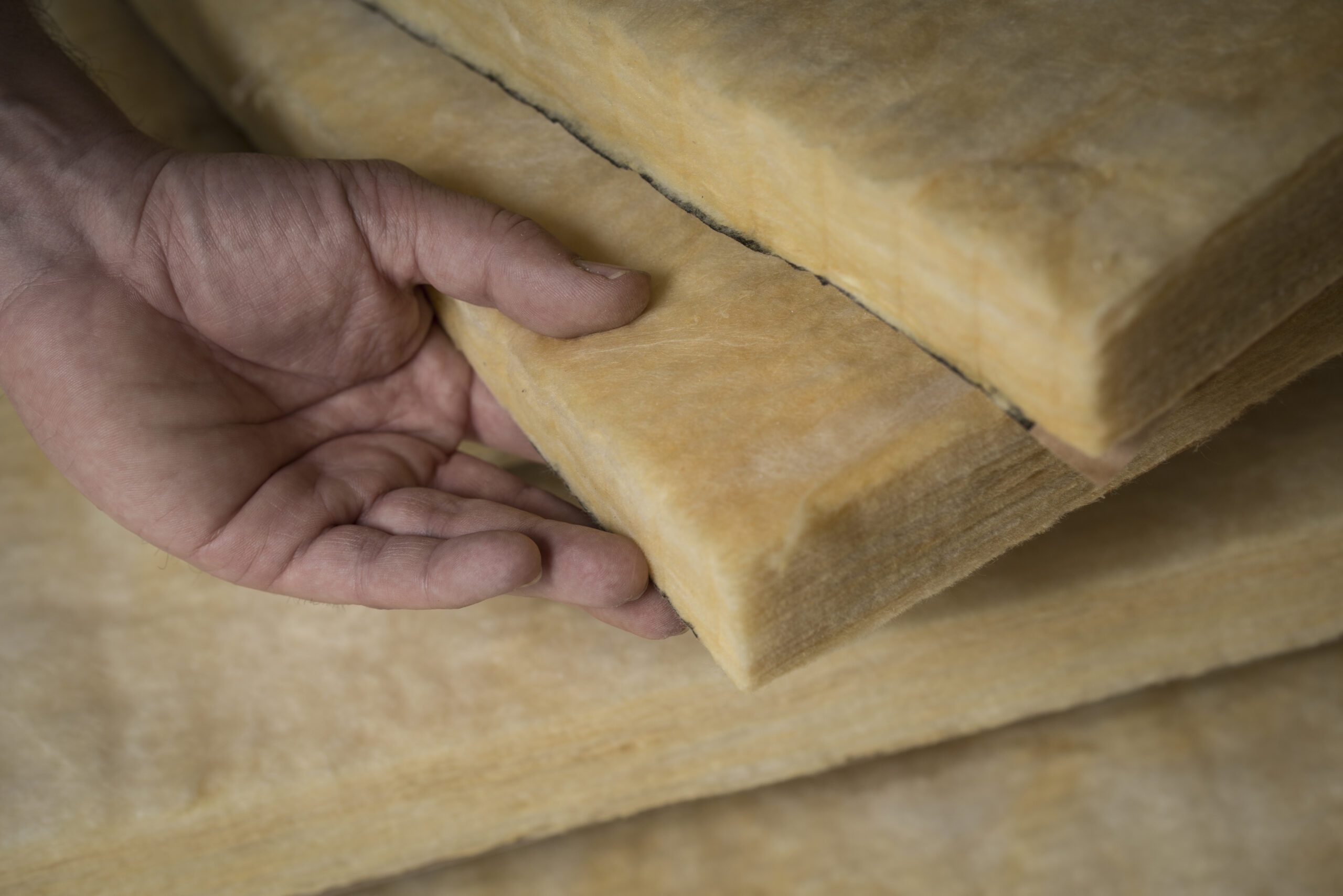 Close-up of a hand pressing on a stack of yellow fiberglass insulation batts.