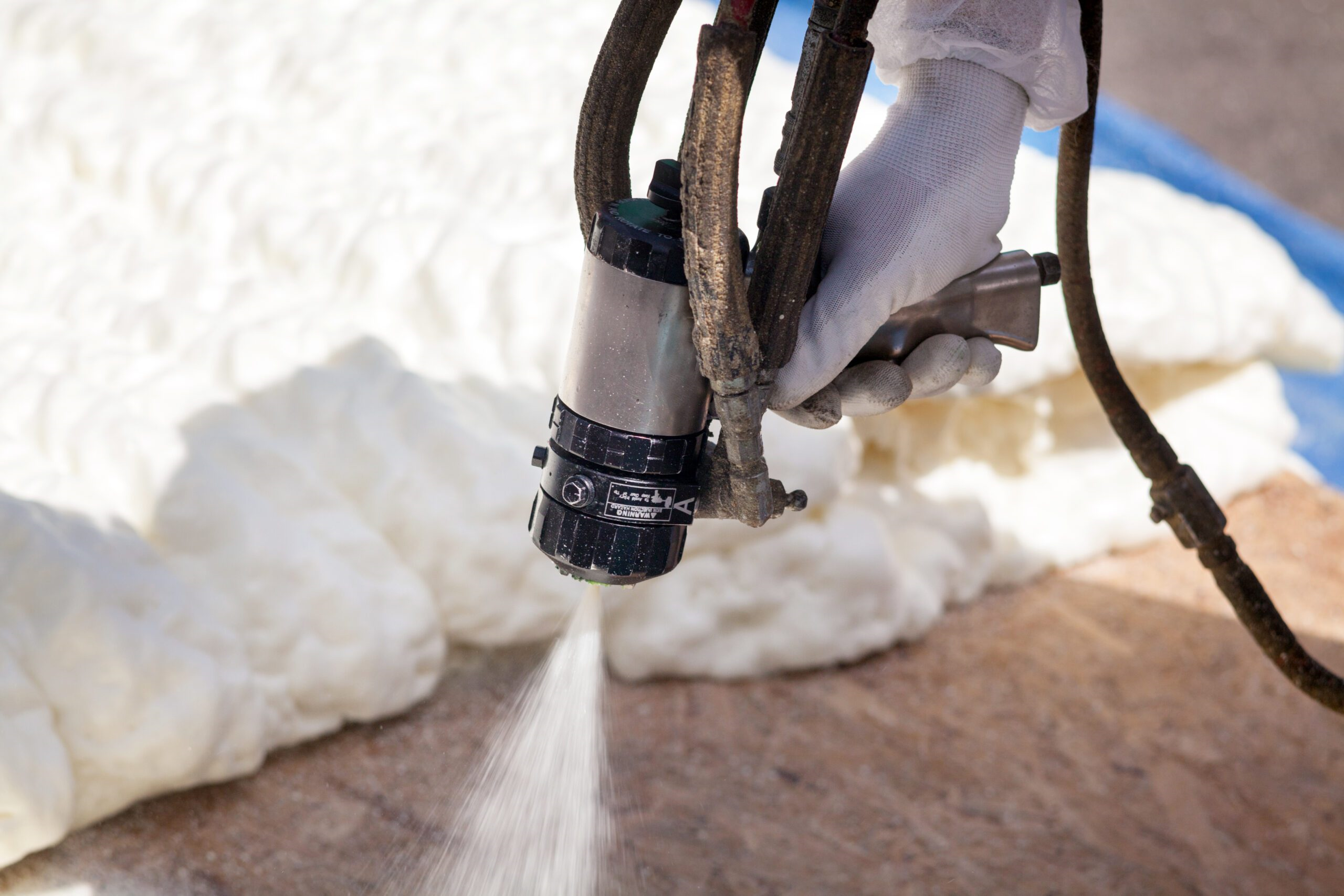 Close-up of a worker's hands applying spray foam insulation with a professional spraying tool.