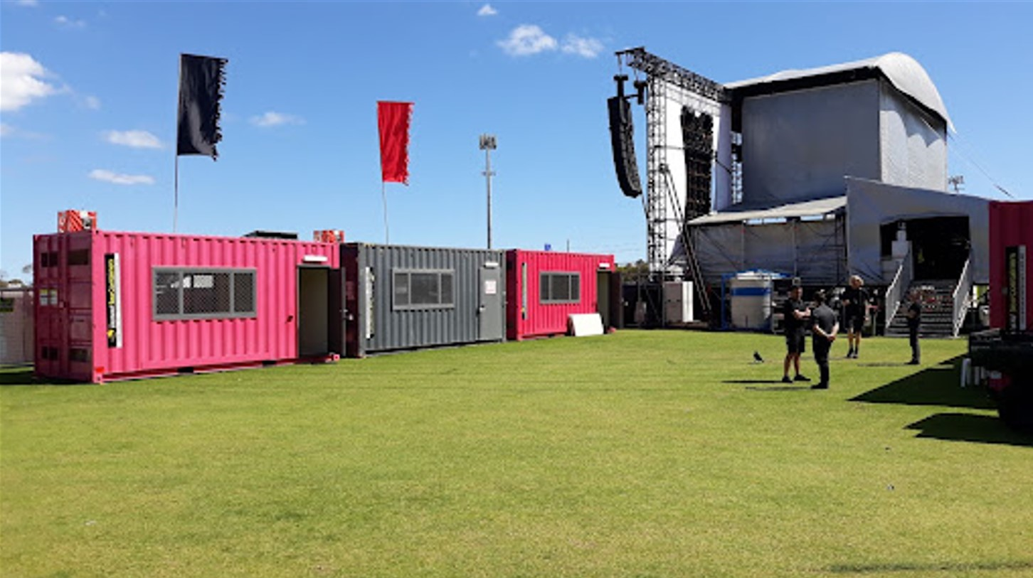 Outdoor event area with colorful shipping containers and a large stage setup on a sunny day with clear skies..