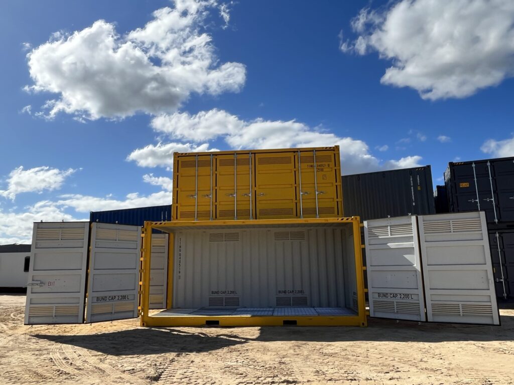 Industrial container with open panels on sandy ground under a bright blue sky.