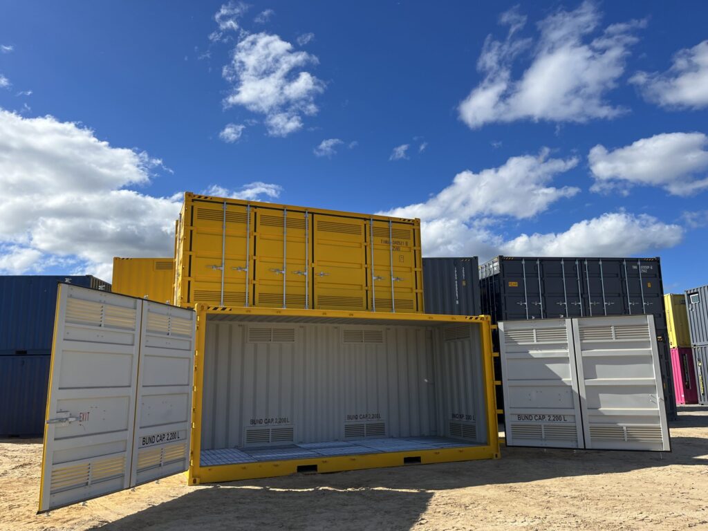 Industrial yard with open and closed yellow containers under a bright blue sky.