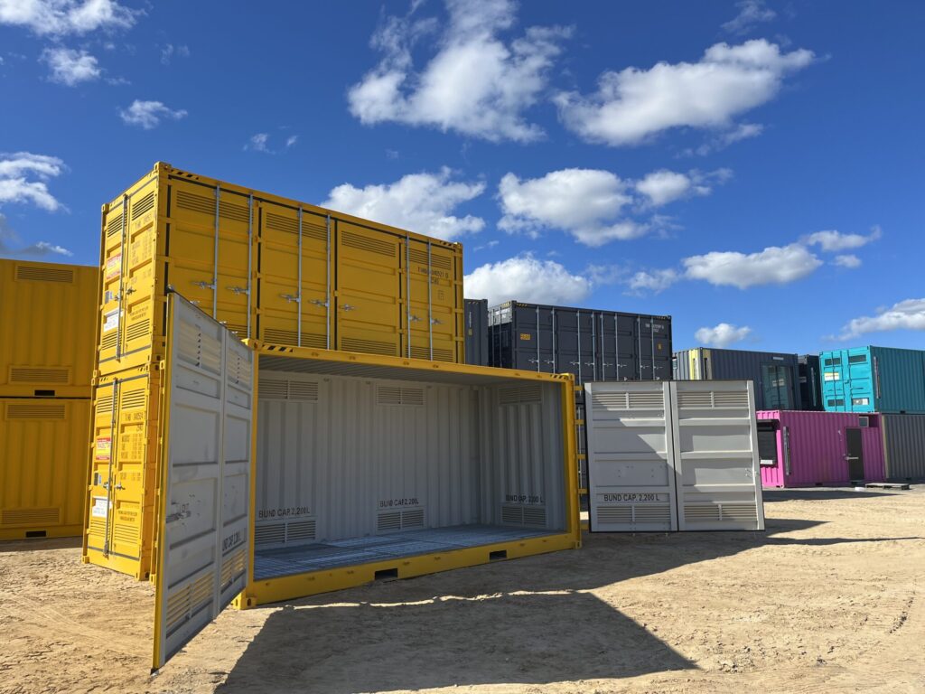 Yellow and blue metal containers stacked neatly in a yard on a sunny day.