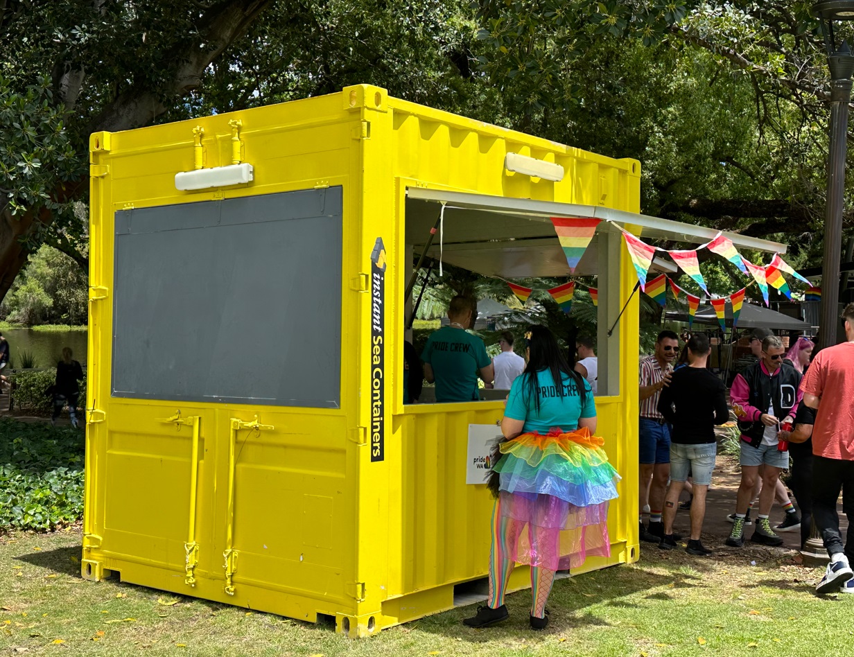 Bright yellow shipping container converted into an outdoor event booth with open serving window and festive decorations.