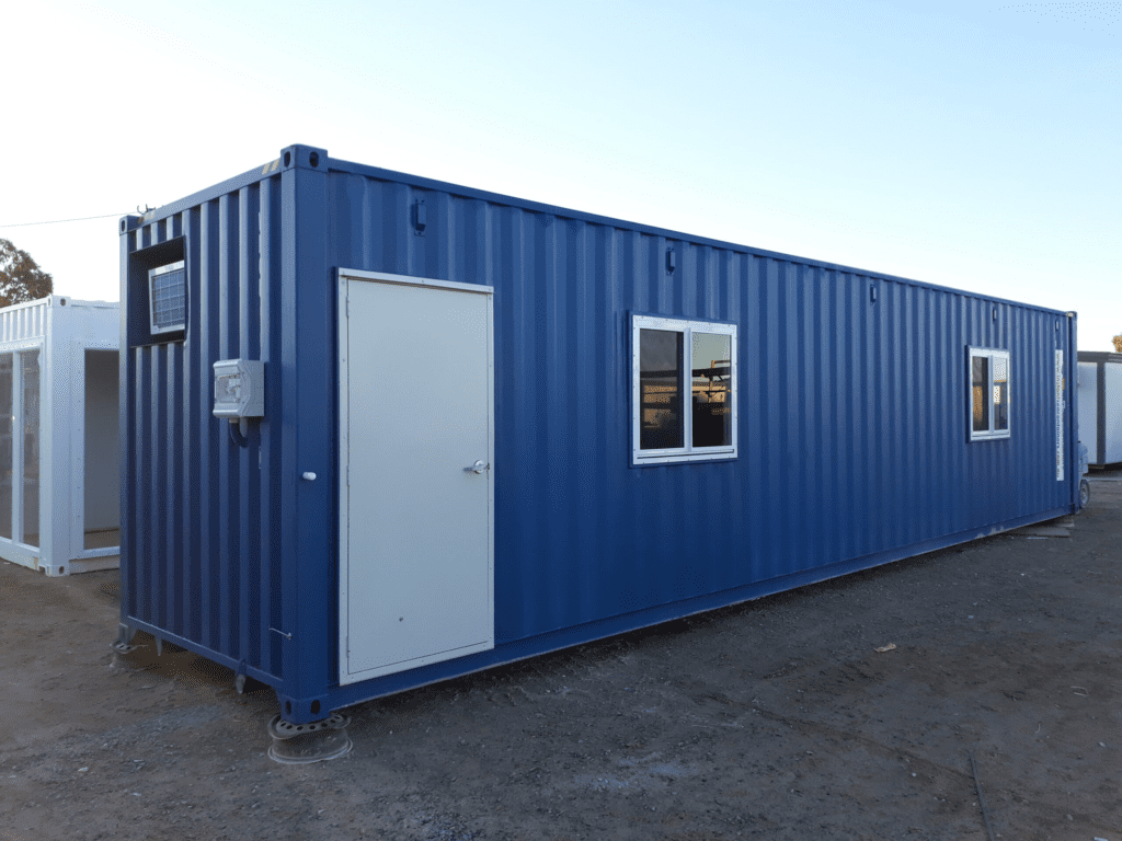 Exterior view of a blue shipping container converted into a portable office with a white door and windows.