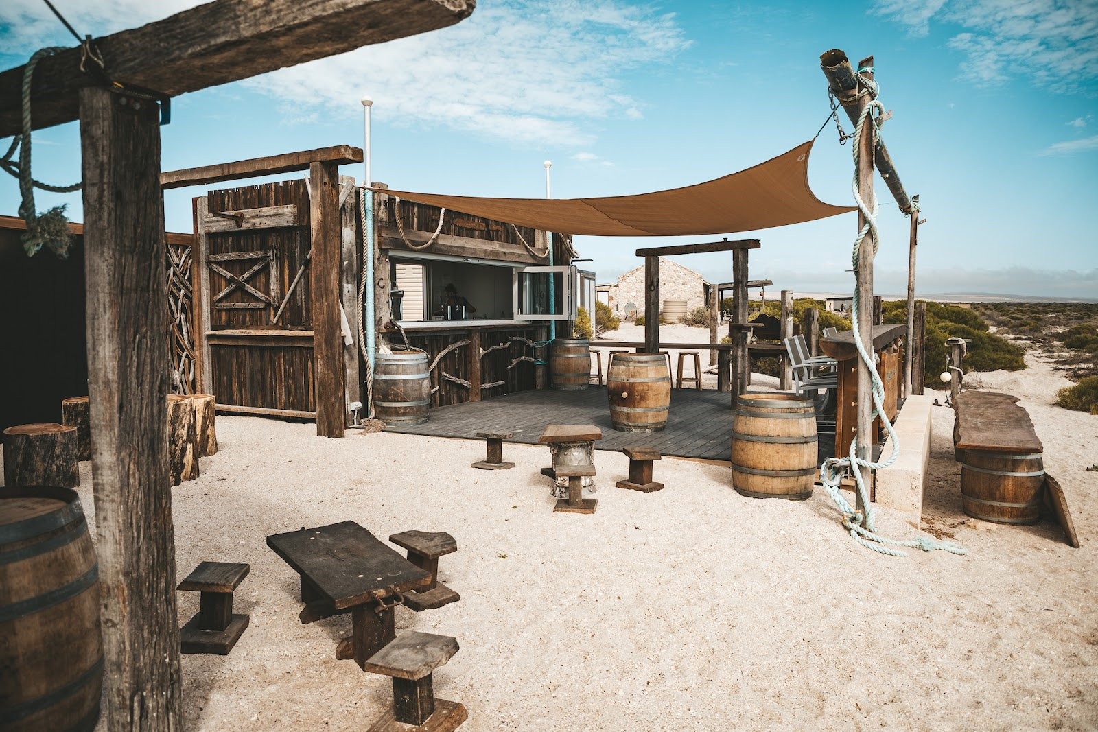Rustic beachside bar setup with wooden structures and barrels.