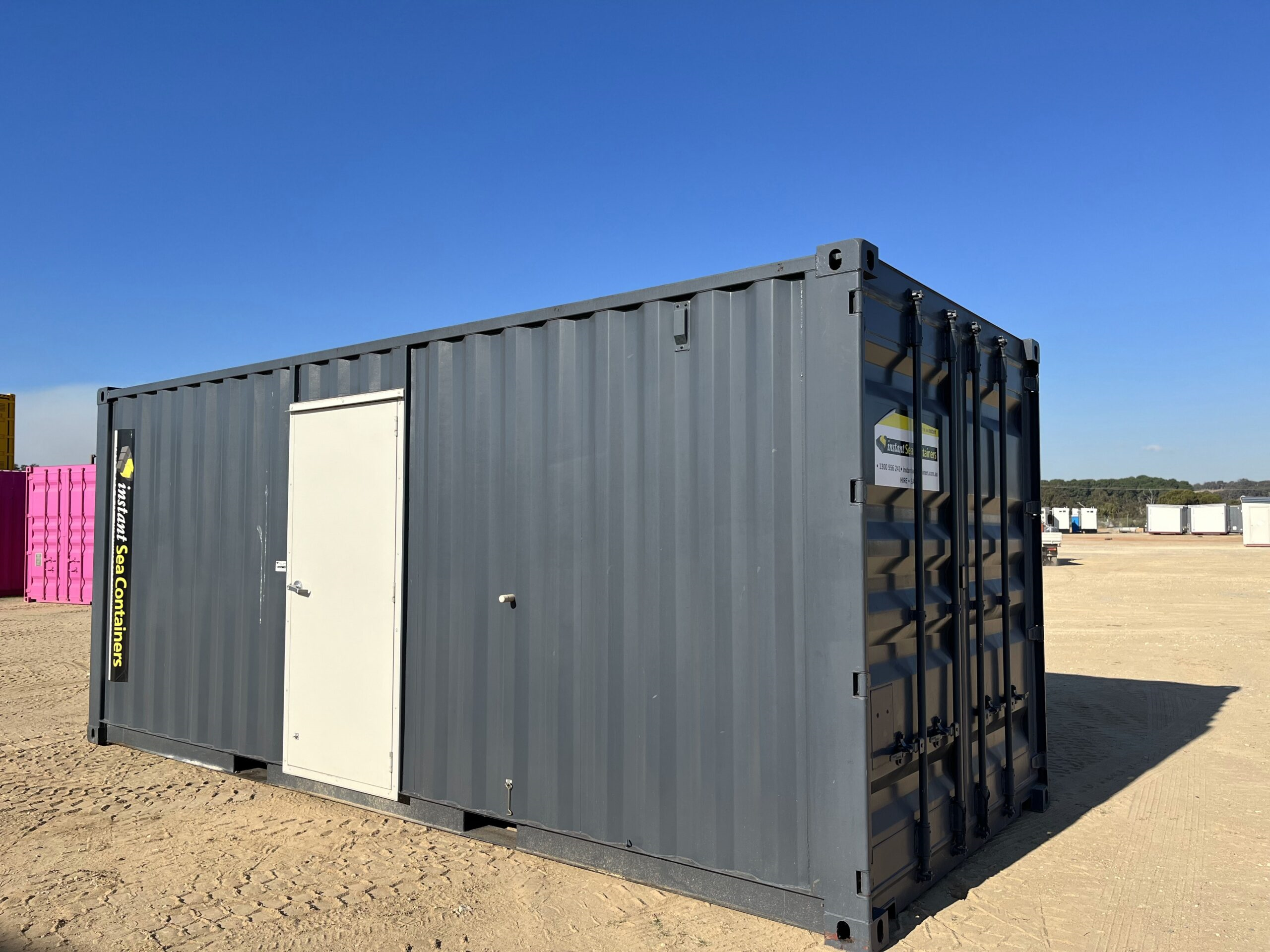 Shipping Container Workshop with a secure door added to one side, situated in a large open area with other containers visible in the background.