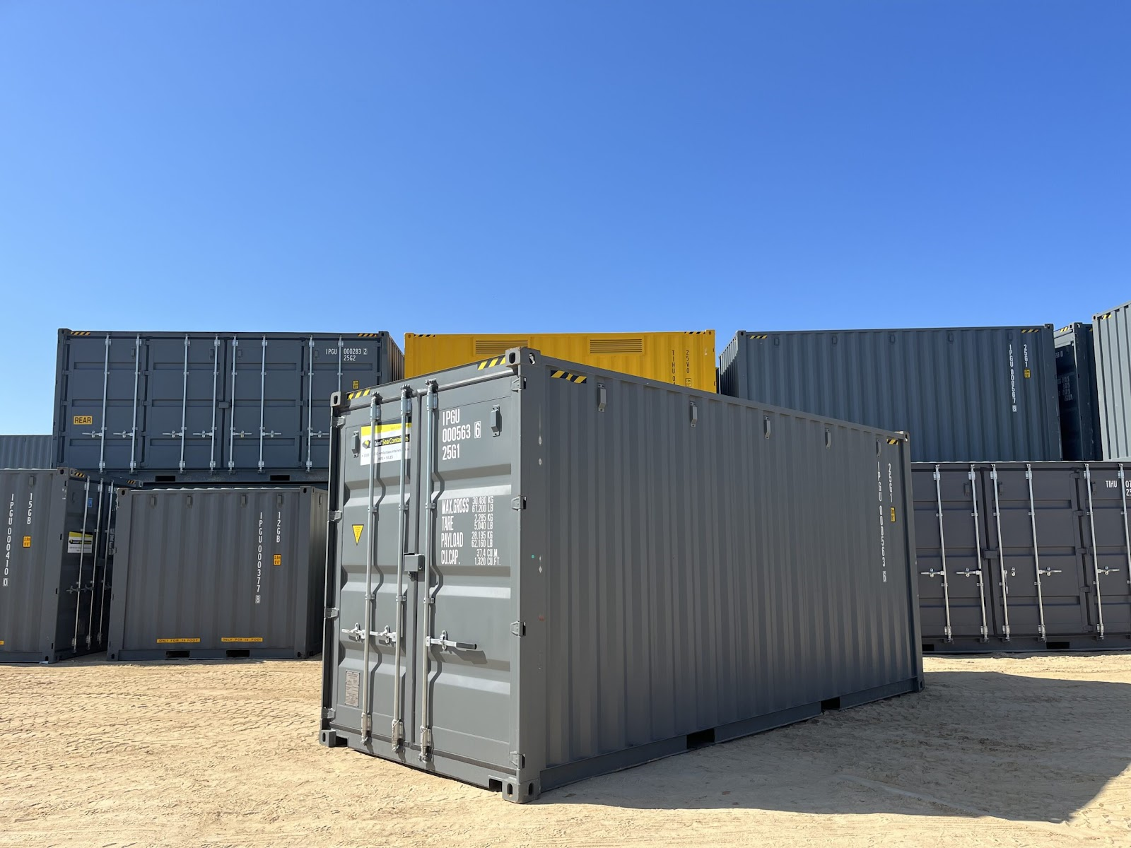Stacked gray and yellow shipping containers in a storage yard under clear blue sky.