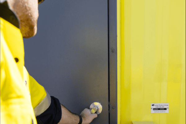 Worker in a high-visibility jacket unlocking a yellow shipping container door.