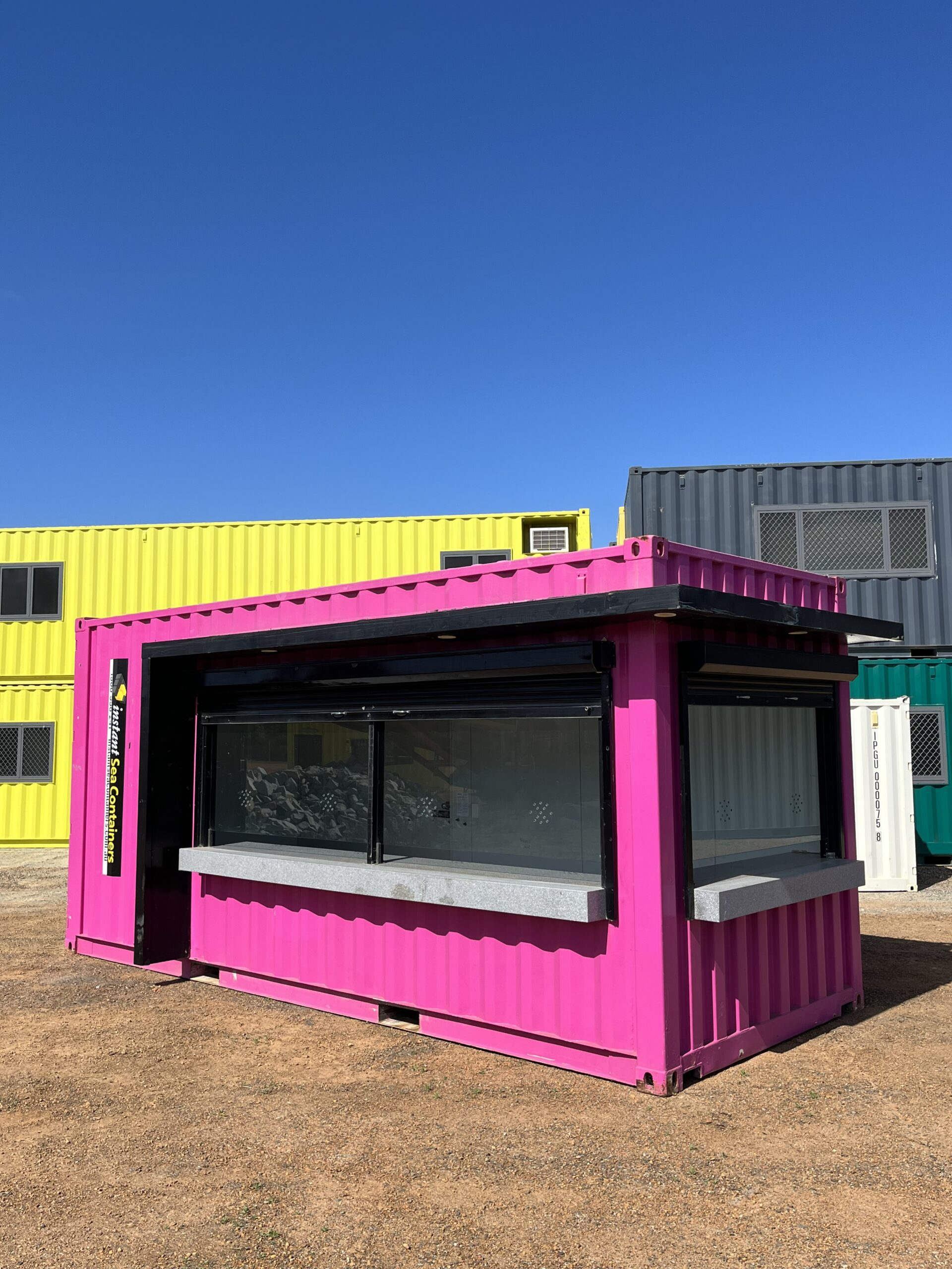 a brightly colored pink Shipping Container Box Office, modified to serve as a retail or food service outlet with large serving window