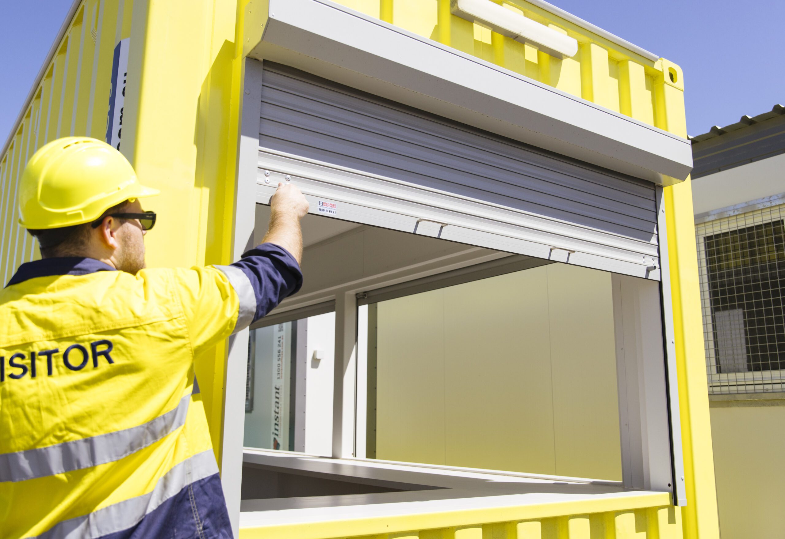 Worker in yellow safety gear adjusting a window shutter on a yellow shipping container