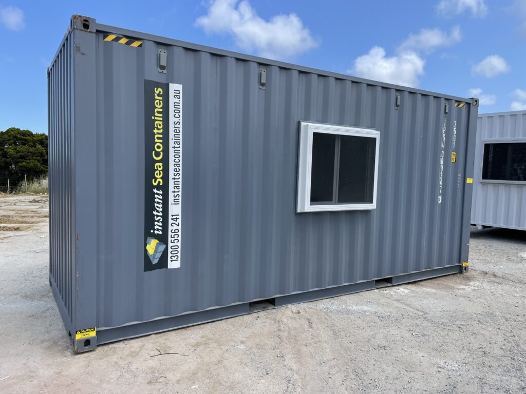 Gray shipping container office with a single window placed outdoors.