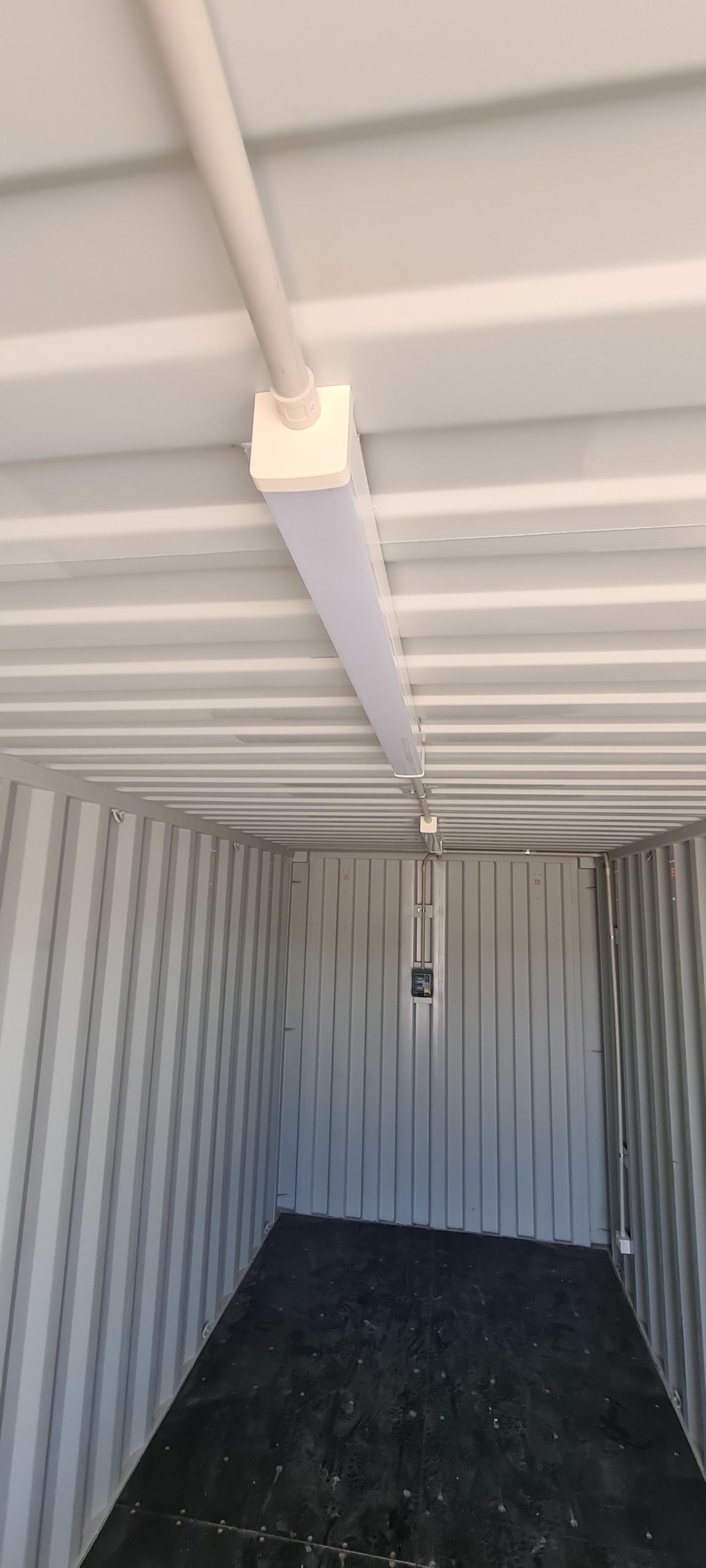 Interior view of empty Shipping Container Storages with mounted overhead lighting and wiring.