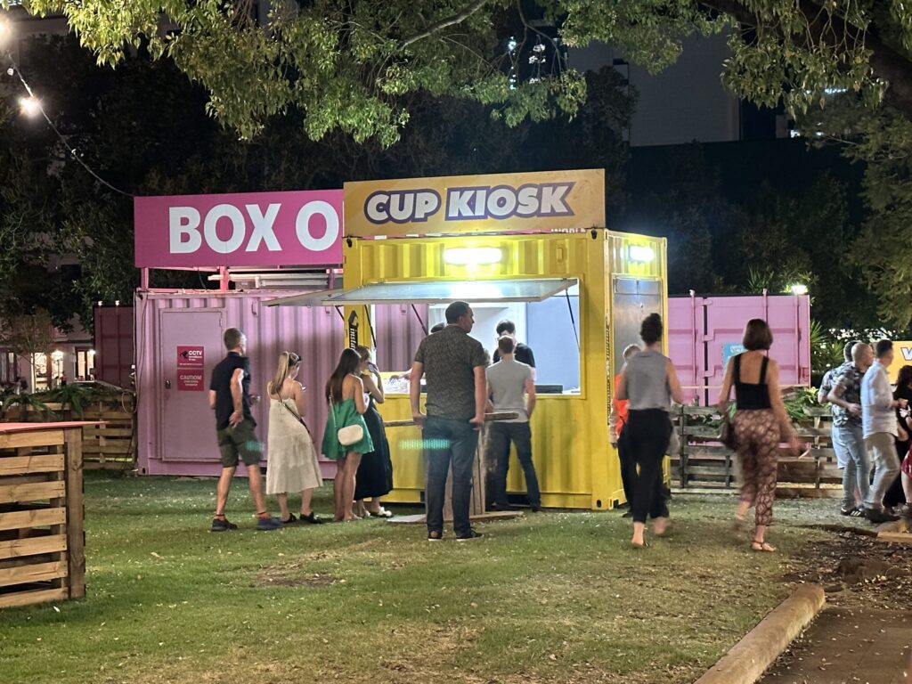 Yellow Cup Kiosk container made from a brightly colored Shipping Containers for Events with people at outdoor nighttime event. (1)